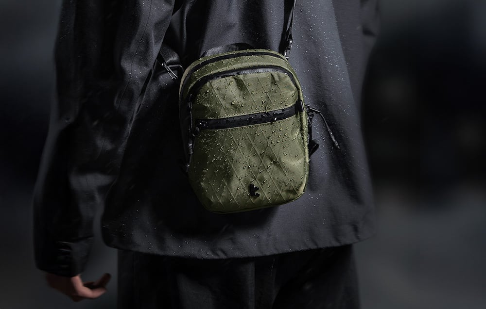 Green bag with water droplets slung over the shoulder of a person in a black jacket