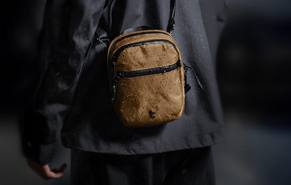 Brązowa torba z kroplami wody przewieszona przez ramię osoby w czarnej kurtce