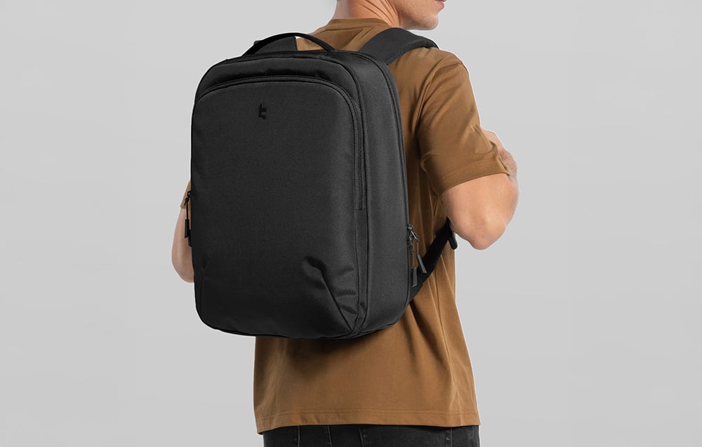 A man in a brown t-shirt wearing a black laptop backpack turned away from the camera