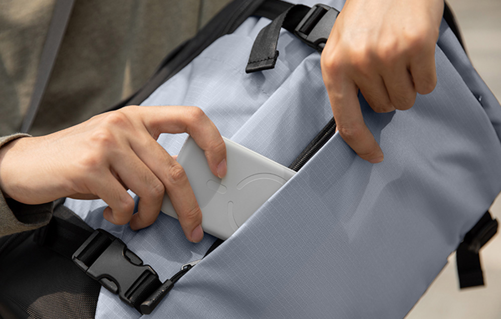 Hands taking a power bank out of the pocket of a gray backpack