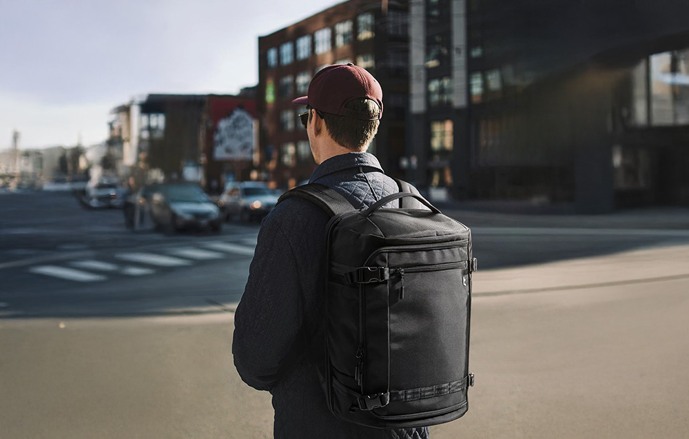 Mężczyzna z czarnym plecakiem Tomtoc Navigator T67 na ulicy miejskiej