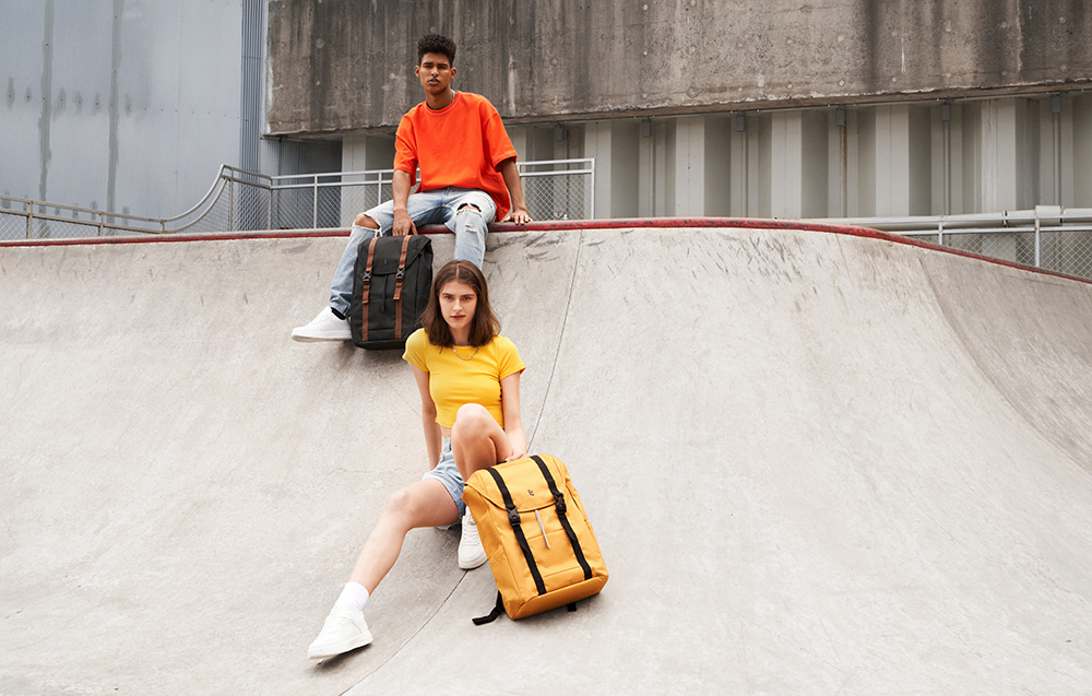 A boy and a girl with backpacks sitting on a ramp at a skate park