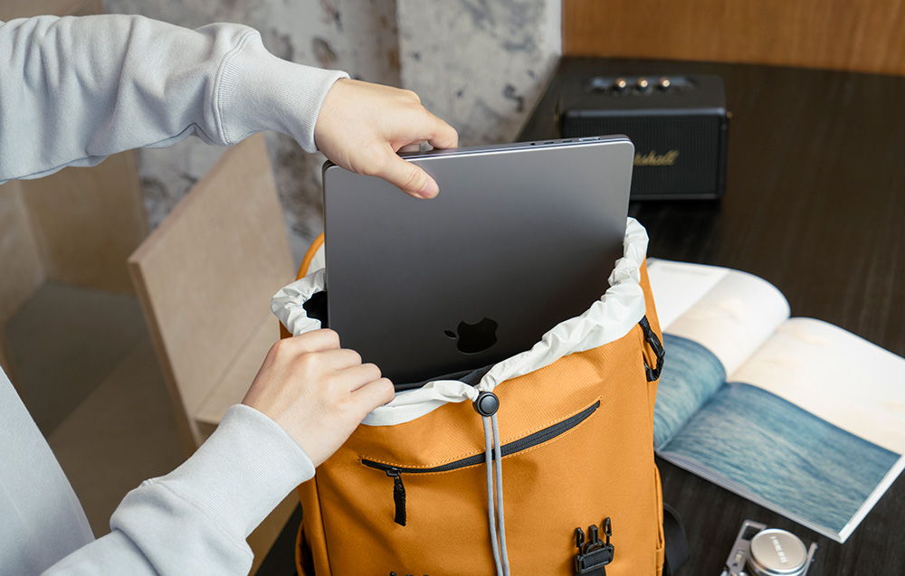 A person in a gray hoodie putting a laptop into a yellow backpack
