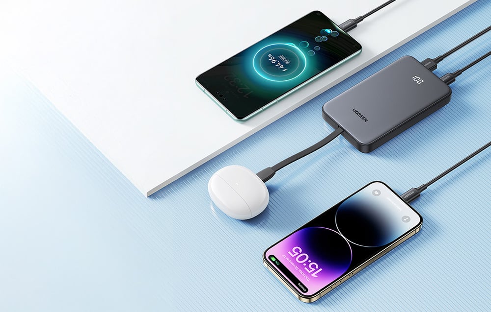 Powerbank Ugreen ładujący jednocześnie trzy urządzenia: dwa smartfony i etui ze słuchawkami bezprzewodowymi.