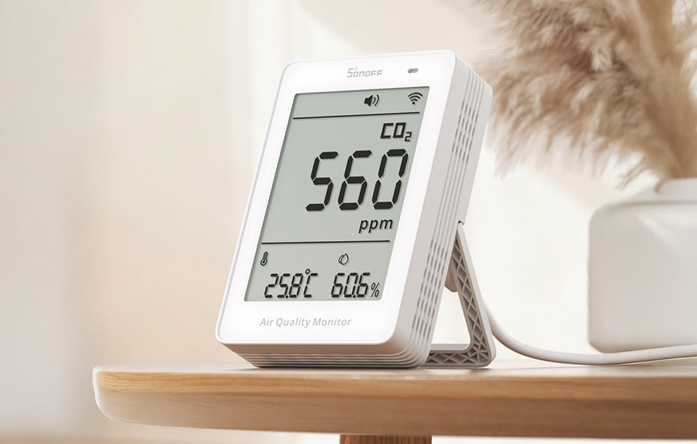 Miernik jakości powietrza Sonoff na drewnianej półce, w tle roślina w wazonie