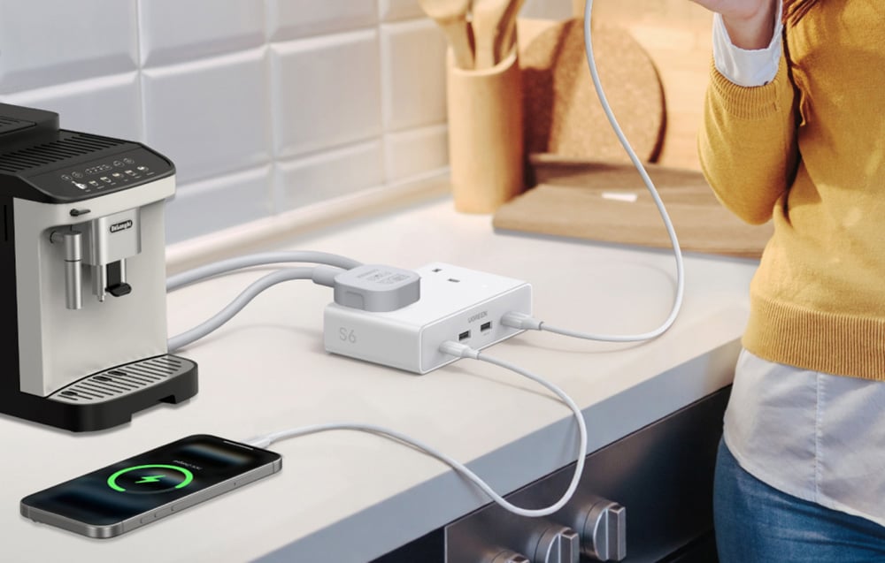 Biała stacja zasilająca na blacie kuchennym, do której podłączony jest ekspres do kawy oraz smartfon.