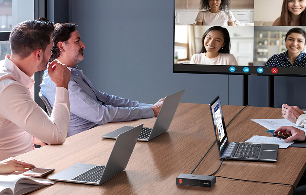 osoby siedzące przy stole z laptopami i rozmawiające przez kamery