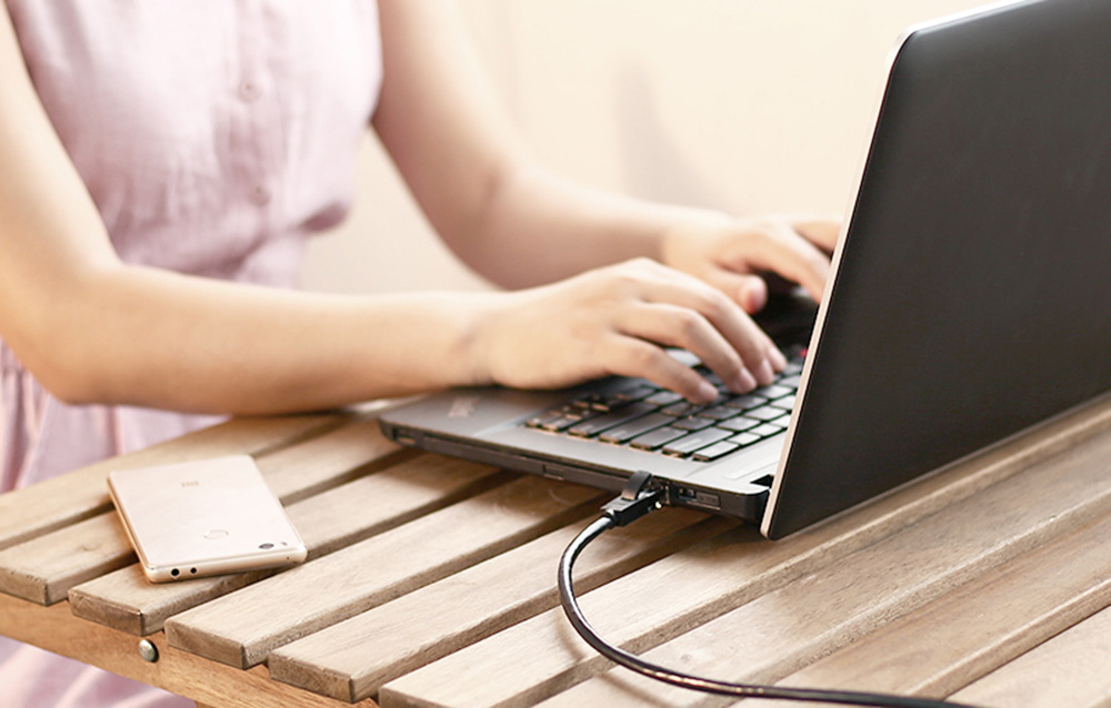 Kobieta w różowej sukience korzysta z laptopa, do kórego podłączono kabel Ethernet