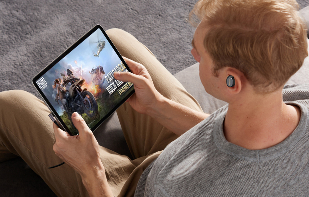 Mężczyzna siedzi na kanapie i gra na tablecie w PUBG Mobile, używając słuchawek dousznych.