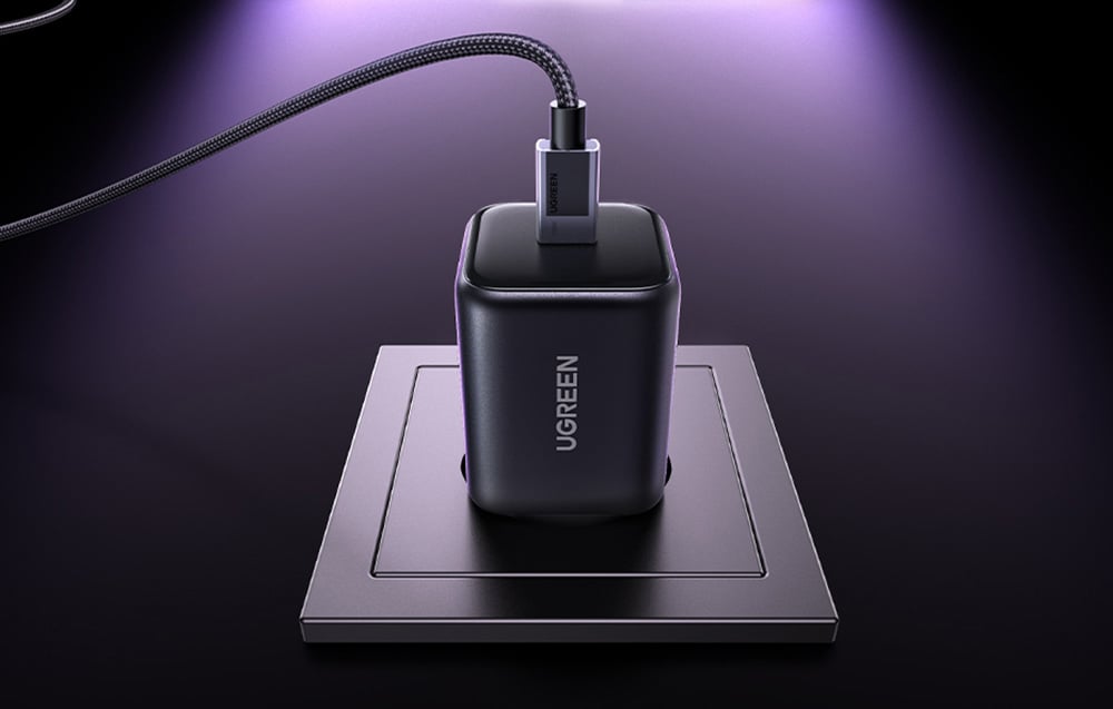 Czarna ładowarka UGREEN z podłączonym kablem USB-C w gniazdku na ciemnym tle.