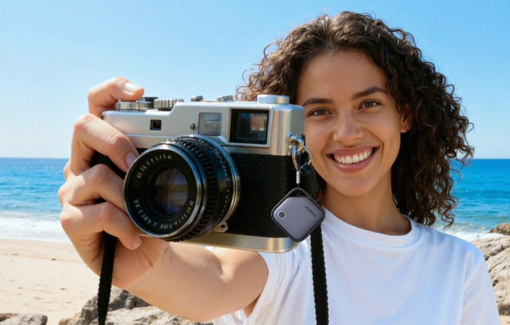 Kobieta na plaży trzyma aparat fotograficzny z przypiętym lokalizatorem UGREEN przy pasku aparatu.