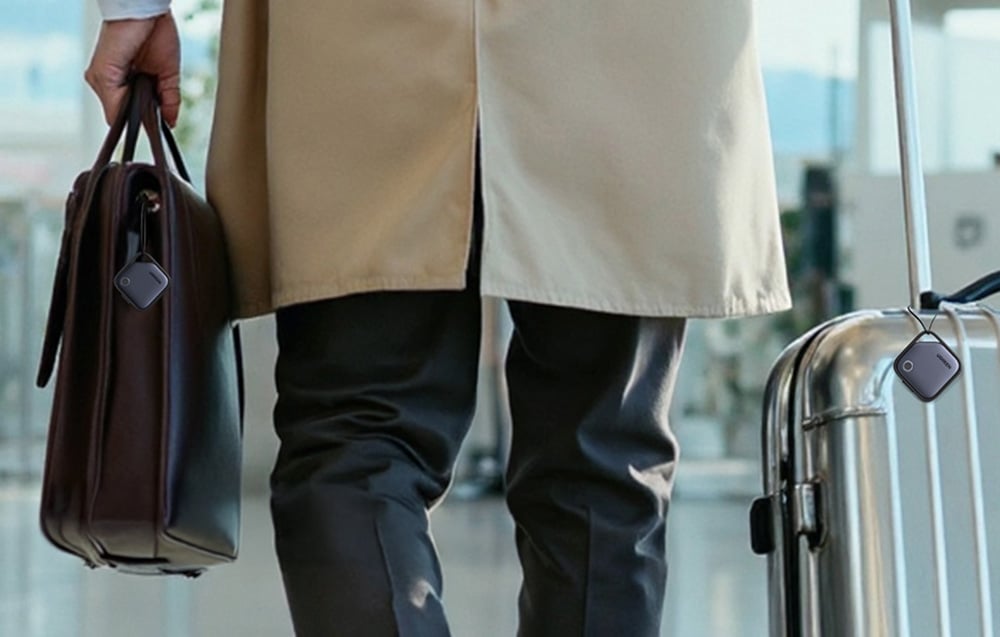 Osoba idzie z torbą i walizką, do których przypięte są lokalizatory UGREEN.