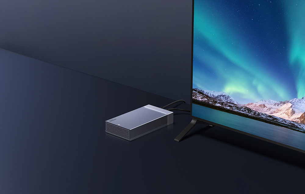 Aluminiowa obudowa dysku UGREEN podłączona do telewizora stojącego na biurku.