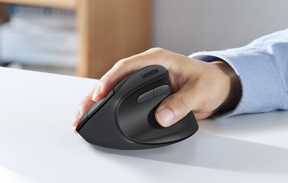 Dłoń trzyma pionową ergonomiczną mysz komputerową UGREEN na białym biurku.