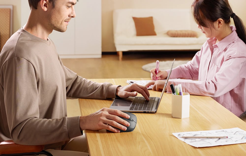 Mężczyzna korzysta z laptopa i pionowej myszy UGREEN przy biurku, podczas gdy dziecko rysuje obok.