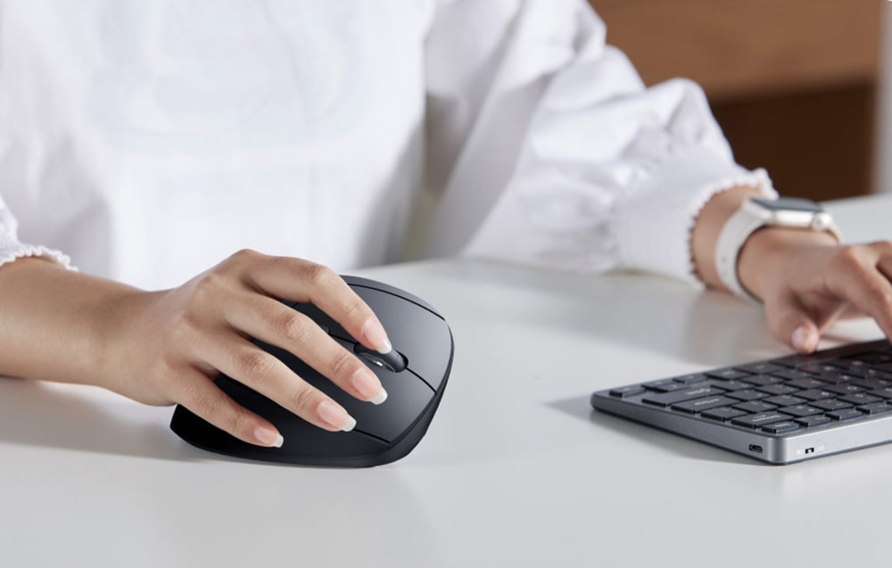 Dłoń korzysta z pionowej myszy UGREEN obok kompaktowej klawiatury na biurku.