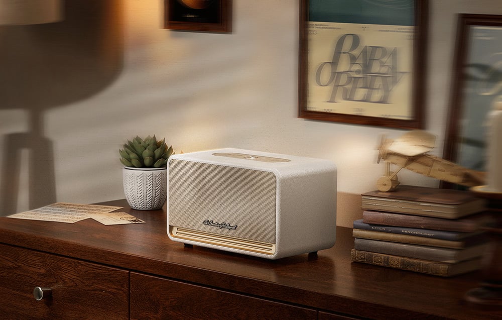 Biały głośnik stoi na drewnianej komodzie obok książek i rośliny w doniczce