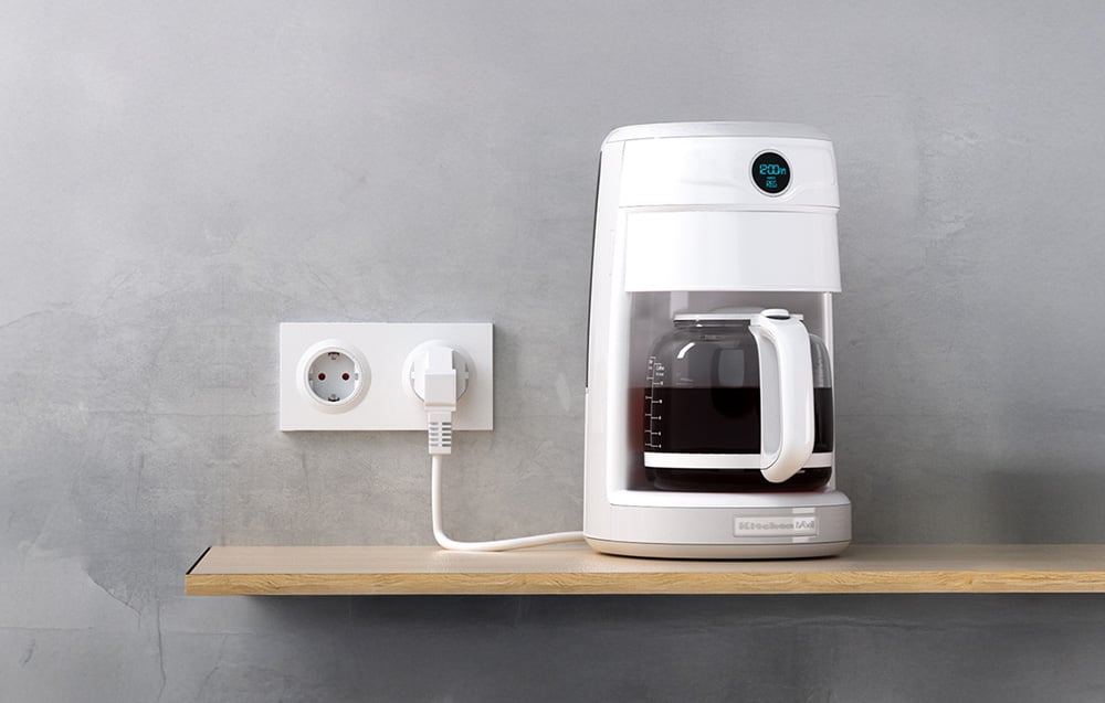 Białe inteligentne gniazdko ścienne Sonoff z podłączonym ekspresem do kawy na drewnianym blacie