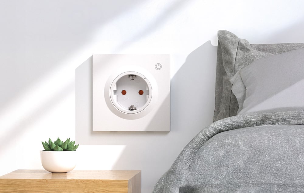 Kwadratowe, białe inteligentne gniazdko podtynkowe zamontowane na ścianie obok łóżka w sypialni
