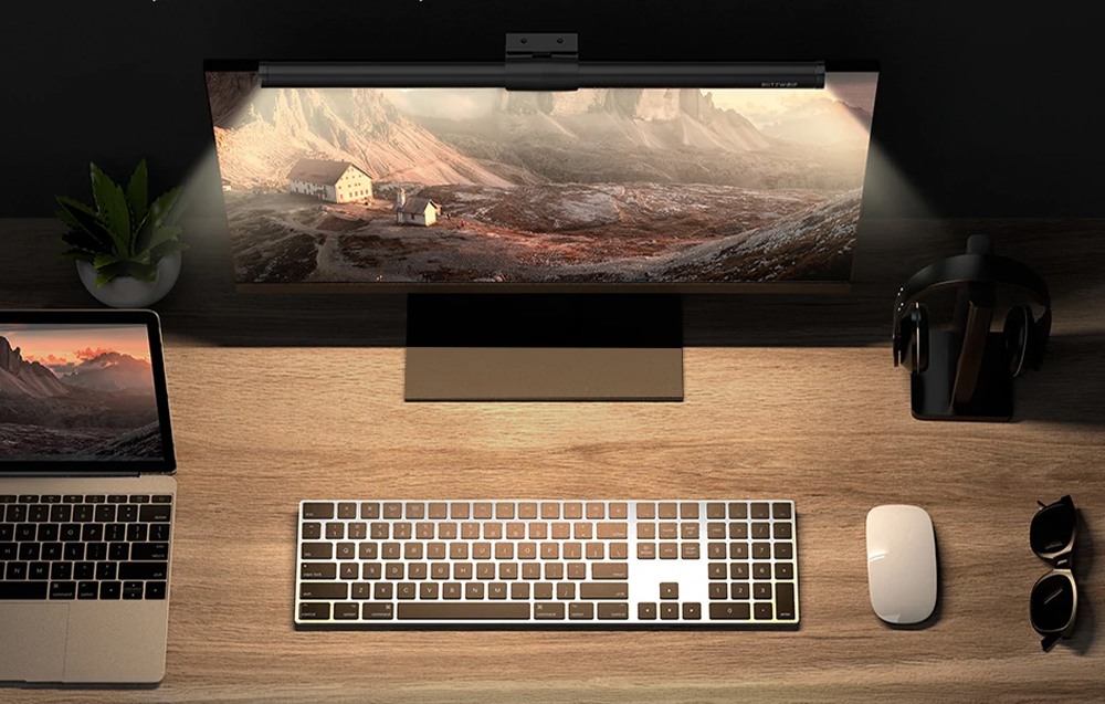 Desk with laptop, keyboard, mouse, and monitor with mounted lamp viewed from above