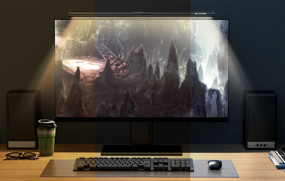 Monitor on desk with lamp attached, next to keyboard, mouse, cup, and glasses