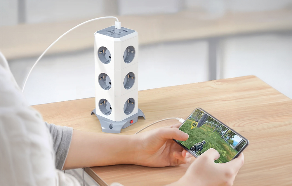 Smartphone held in hands with a game running connected to a power strip lying on a wooden table