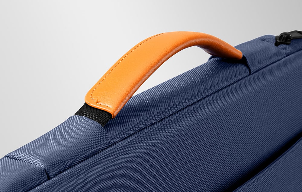 Zbliżenie na pomarańczowy uchwyt i czarny suwak granatowego etui na laptopa