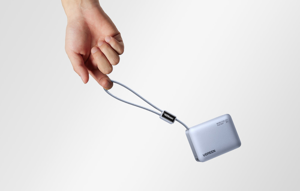 Szary powerbank Ugreen trzymany za wbudowany kabel w ręce