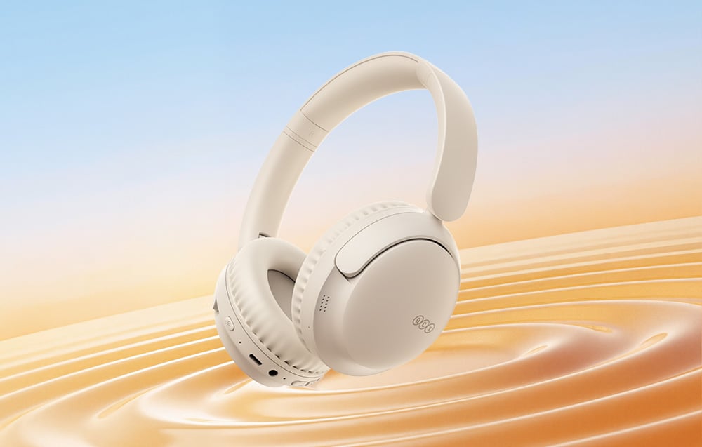 Kremowe słuchawki bezprzewodowe z logo QCY unoszące się nad falistą powierzchnią