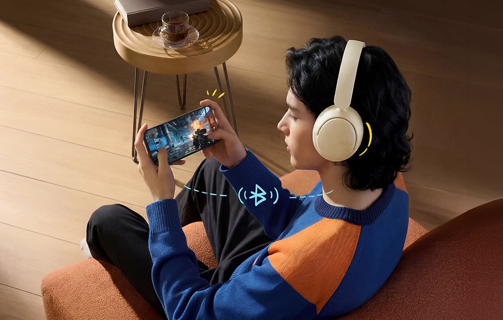 Młody mężczyzna w słuchawkach gra w grę na smartfonie, widoczny symbol Bluetooth