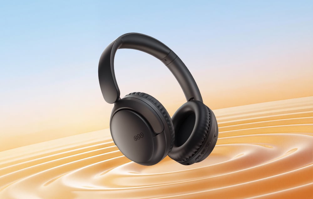 Bezprzewodowe słuchawki nauszne w czarnym kolorze, unoszące się nad falującą, złotą powierzchnią