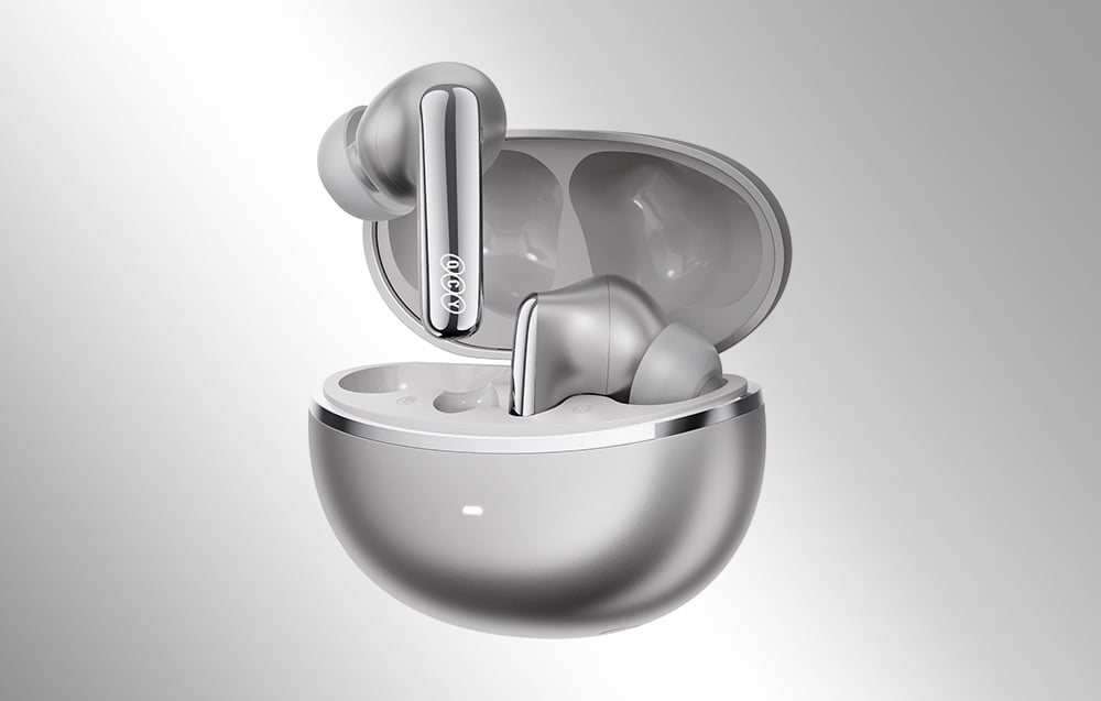 Srebrne słuchawki douszne QCY wystające z otwartego, metalicznego etui ładującego na jasnym tle