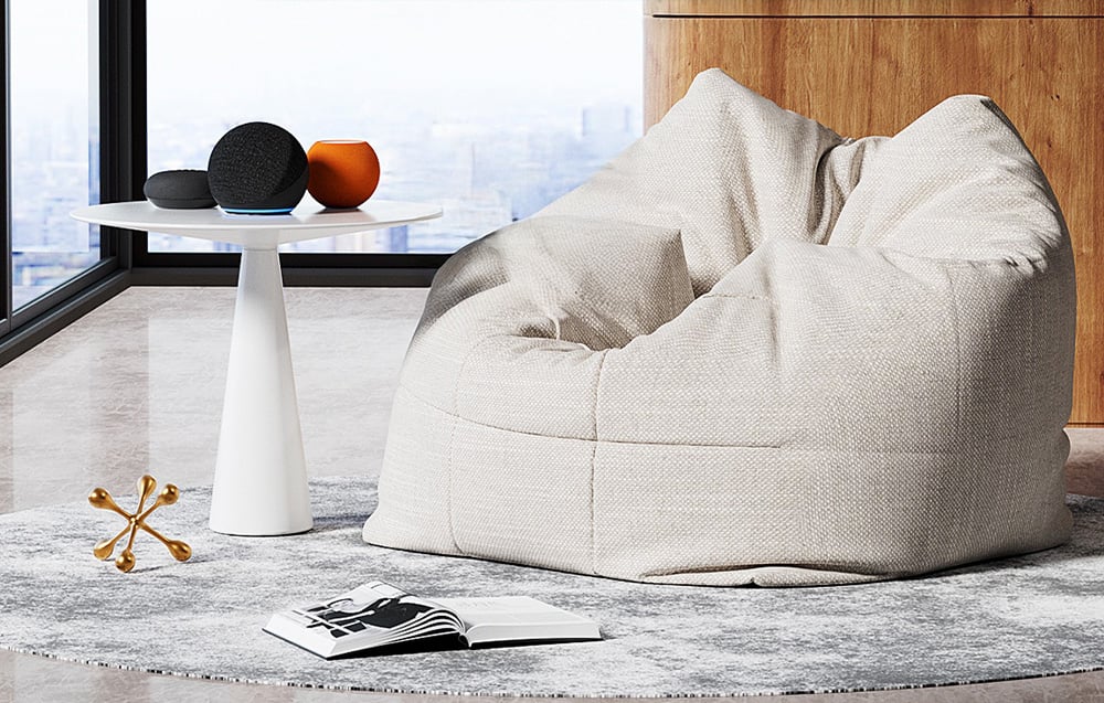 Szara pucha w salonie obok białego stolika z ozdobami przy dużym oknie, na dywanie otwarta książka