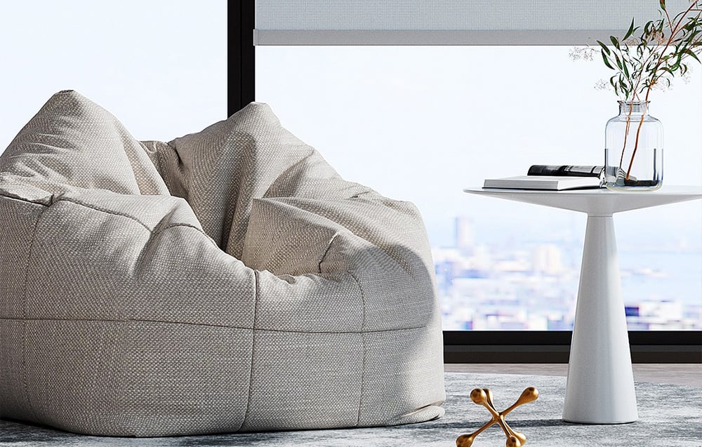 Szara pucha w salonie obok białego stolika z ozdobami przy dużym oknie z roletą