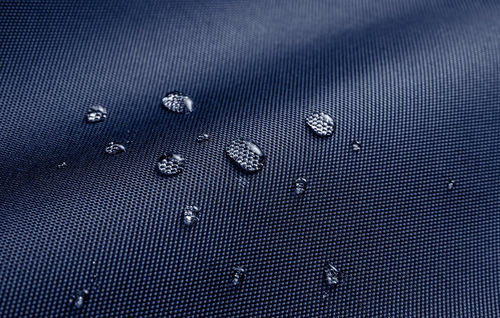 Close-up of water droplets on waterproof, navy material with a distinct weave