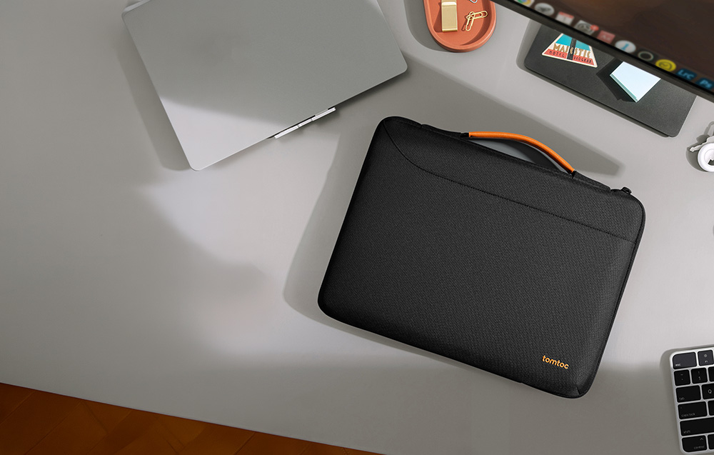 Widok z góry na czarne etui na laptopa z pomarańczową rączką, leżące na biurku