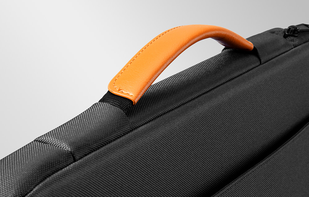 Zbliżenie na pomarańczową, skórzaną rączkę przymocowaną do czarnego etui na laptopa.