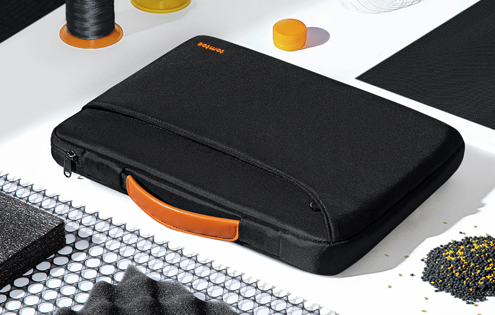Czarne etui na laptopa leżące na jasnym blacie w otoczeniu materiałów produkcyjnych, takich jak nici i granulat