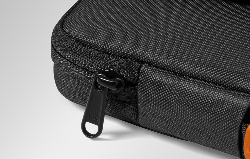 Detal czarnego zamka błyskawicznego YKK wszytego w krawędź ciemnego etui na laptopa
