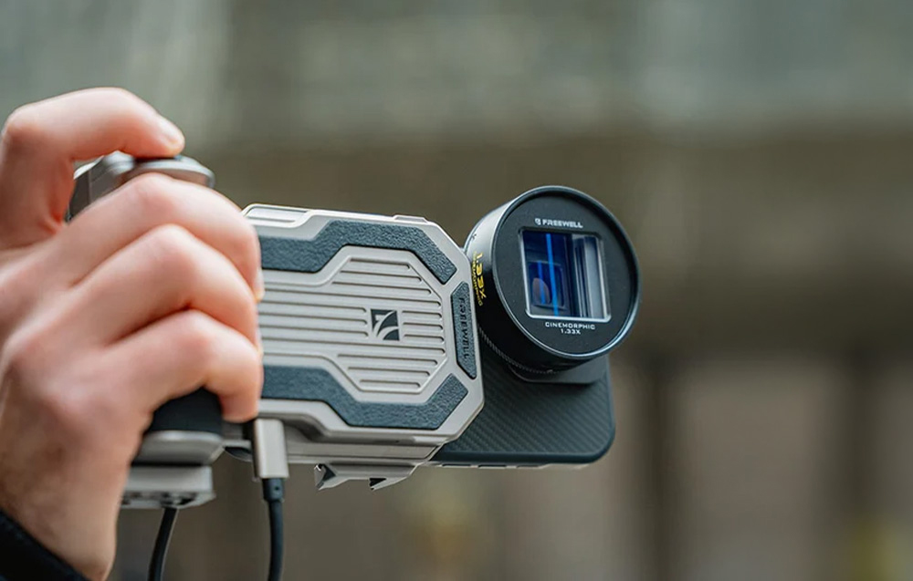 Anamorphic lens mounted on a smartphone in a professional grip with a shutter button and cable.
