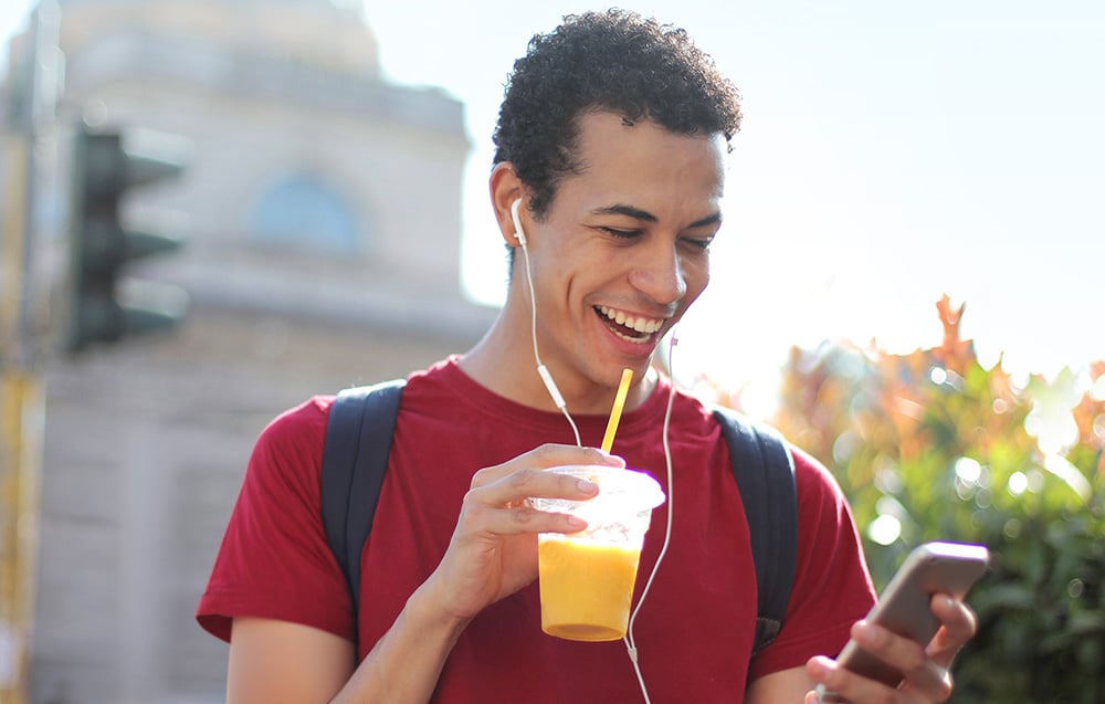 Usměvavý muž se smartphonem a šálkem s džusem v ruce