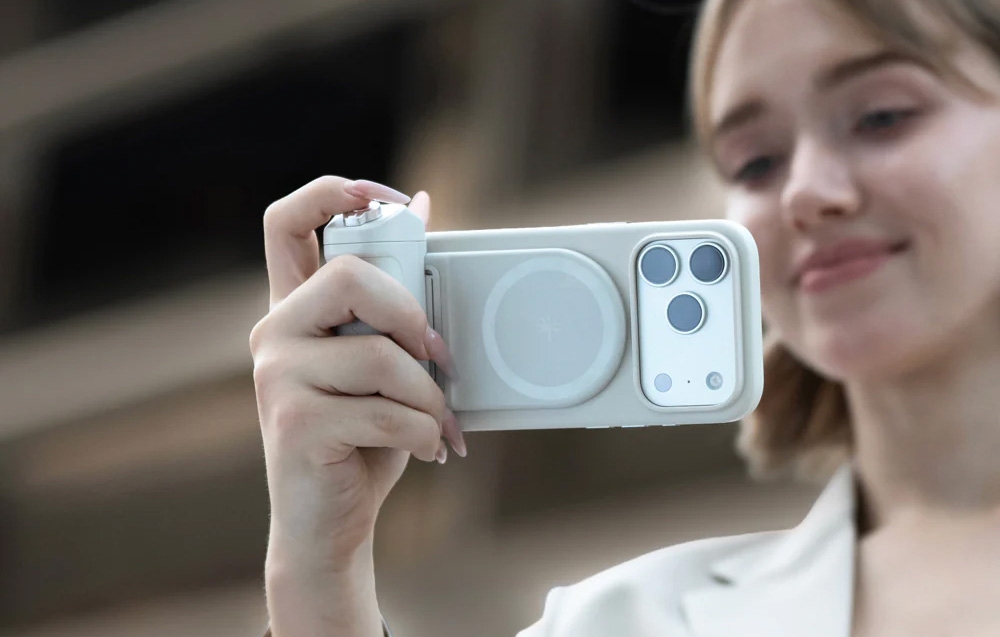 A woman holding a smartphone with the attached grip and taking a photo outdoors