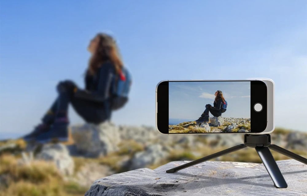 Smartfon na statywie nagrywający osobę siedzącą na skale w plenerze