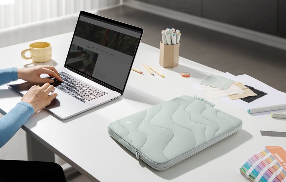 Husa quilted mint cu laptopul stând pe un birou alb lângă o persoană care lucrează la un computer MacBook