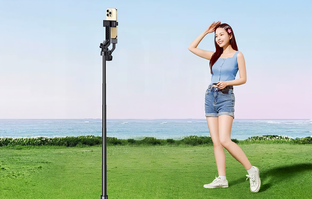 Woman posing on the grass by the sea in front of a phone placed on a tall tripod