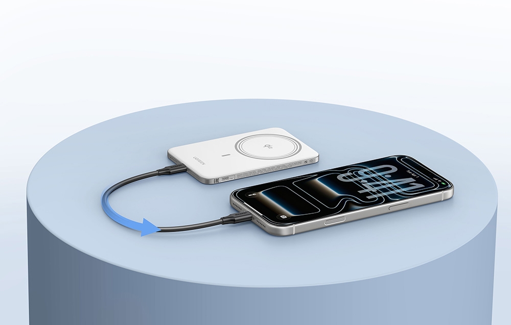White power bank connected with a black cable to a smartphone lying next to it on a blue table