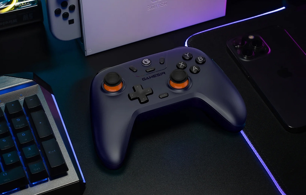 Czarny kontroler do gier leżący na biurku obok klawiatury, telefonu i konsoli Nintendo Switch