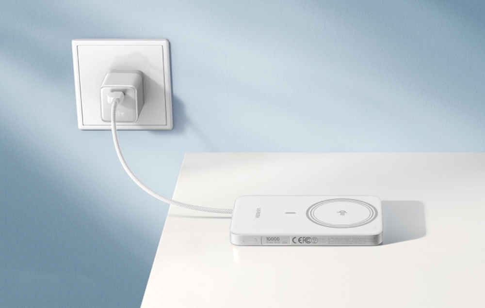 A white Ugreen power bank lying on a white table connected to a power outlet