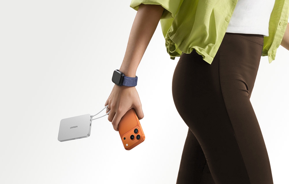 A woman in a green shirt holding an orange smartphone and a white Ugreen power bank