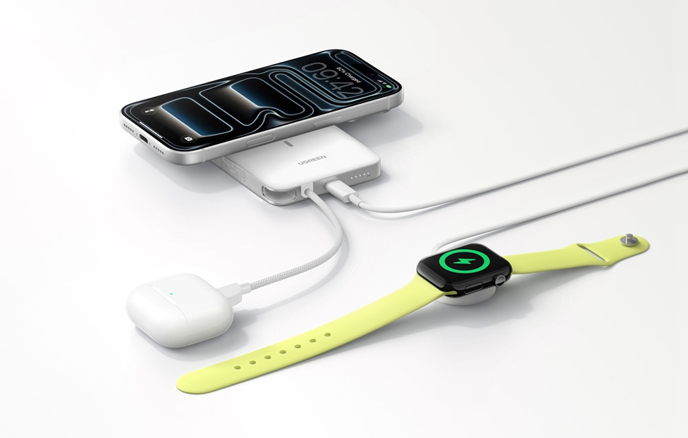 A smartphone, TWS headphones, and a smartwatch connected to a white Ugreen power bank lying on a table